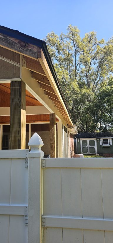 Side view of a house with a wooden porch and a white fence in the foreground.